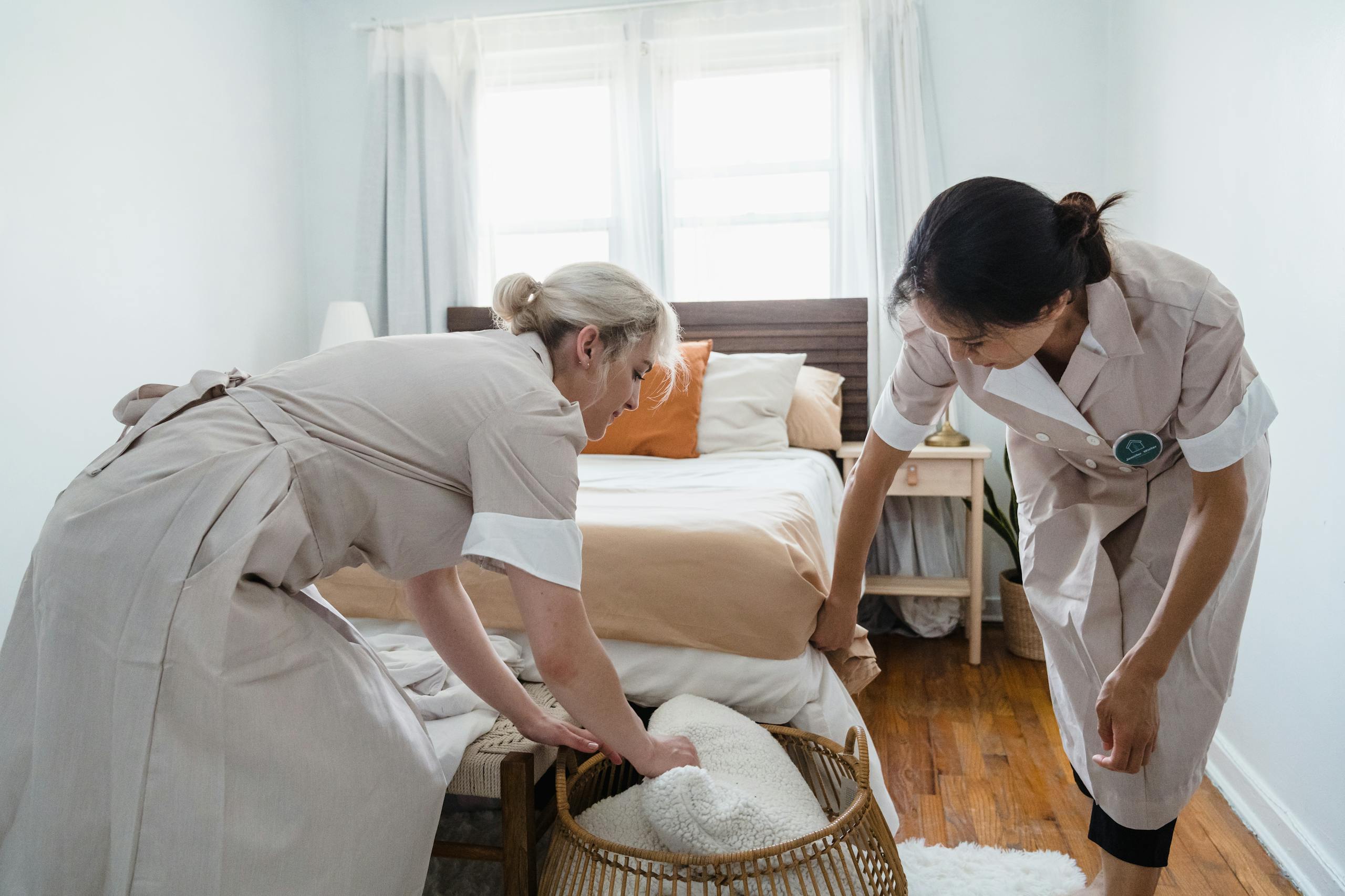 Two housekeepers organizing a bedroom, focusing on tidiness and comfort.